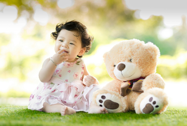 baby girl sitting next to a teddy bear